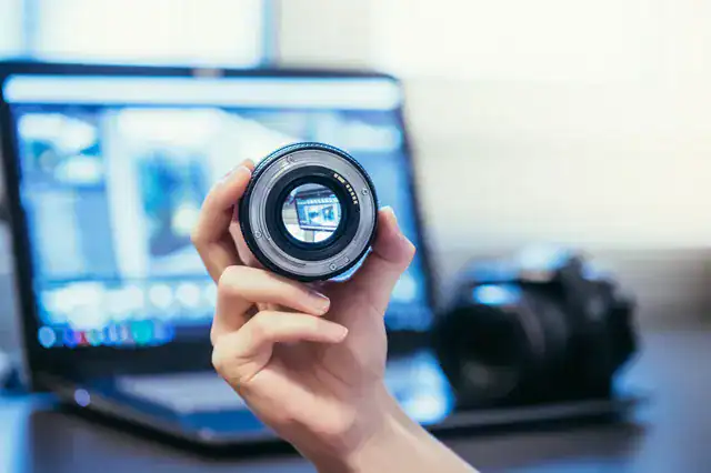 photographer-holding-lens-camera-laptiop